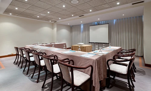 Sala de conferencias con mesa en U y proyector al frente.