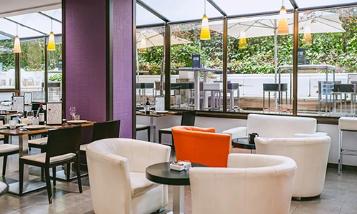 Sala de restaurante con sillas blancas y naranjas y grandes ventanas.