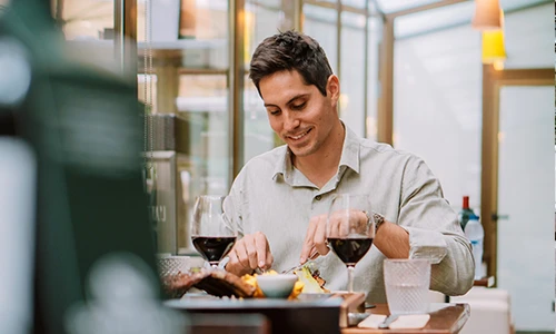 Hombre sonriendo mientras cena con vino en un restaurante elegante.