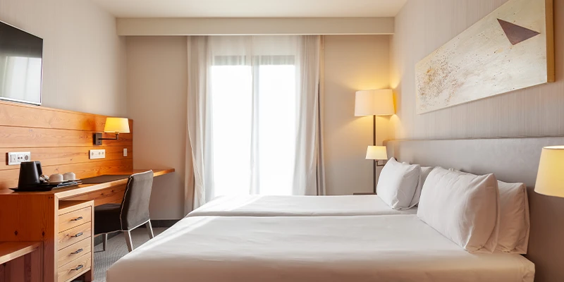 Habitaci&oacute;n moderna y luminosa con dos camas y escritorio de madera.