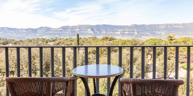 Vista desde el balc&oacute;n con sillas y mesa hacia monta&ntilde;as y cielo azul.