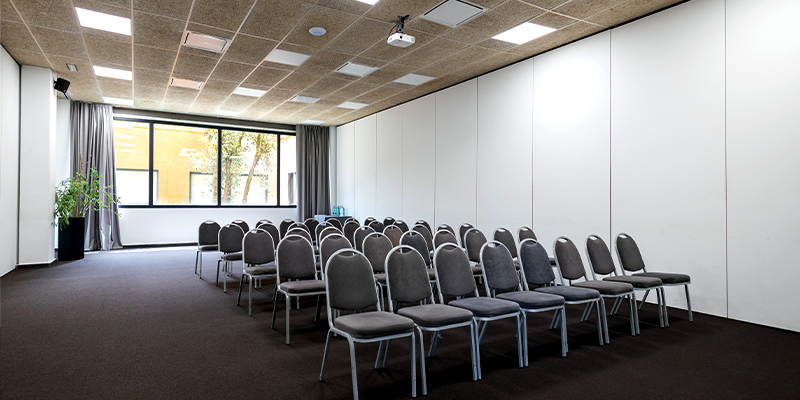 Sala de conferencias vac&iacute;a con sillas alineadas y ventana amplia.
