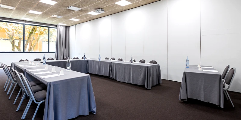 Sala de conferencias vac&iacute;a con mesas y sillas dispuestas en forma de U.