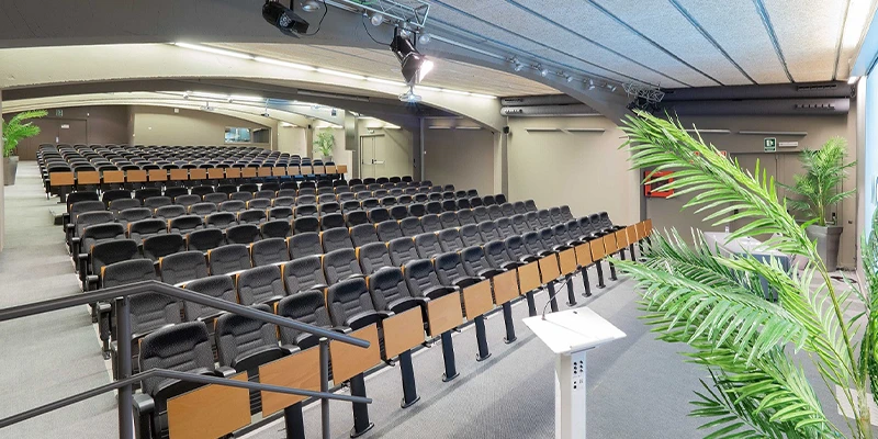 Sala de conferencias vac&iacute;a con filas de asientos y un podio.