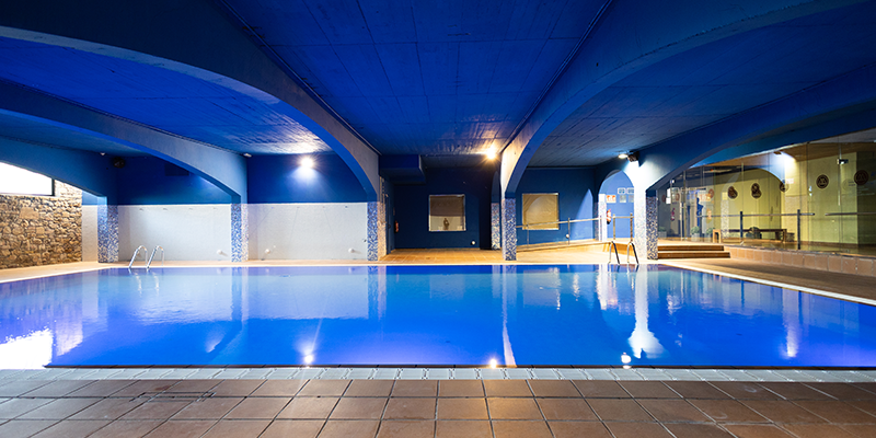 Piscina cubierta con iluminaci&oacute;n azul y techo abovedado.