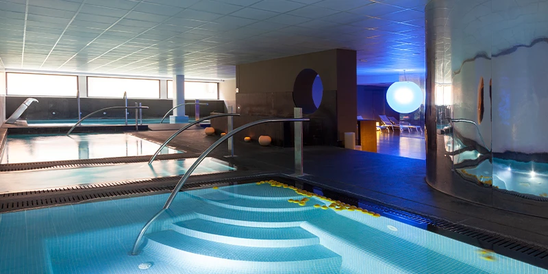 Piscina interior iluminada con chorros de agua y luz azul suave.