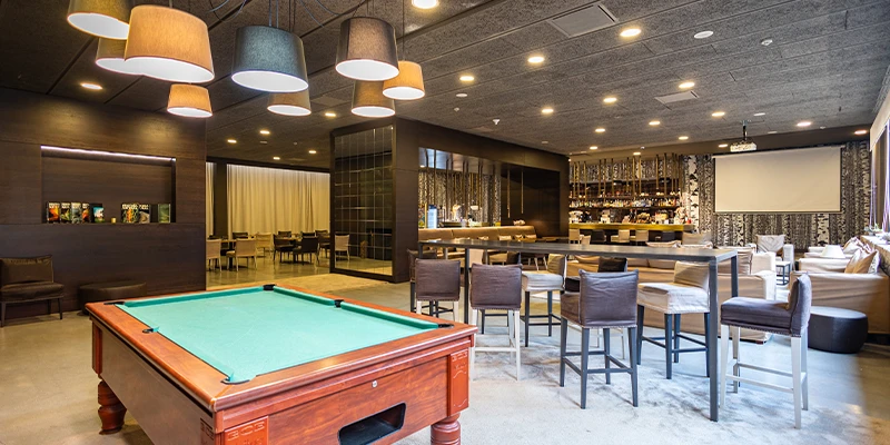 Sala de juegos con mesa de billar, bar y c&oacute;modos asientos iluminados.