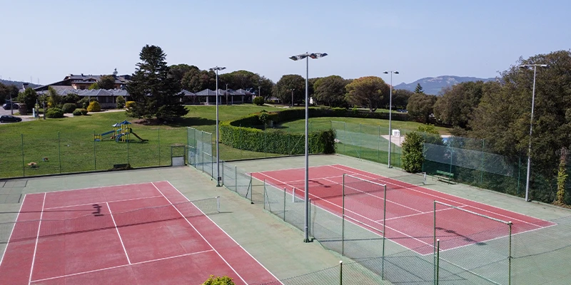 Dos canchas de tenis al aire libre junto a un &aacute;rea verde y un parque infantil.