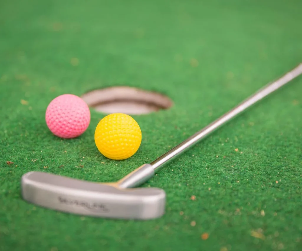 Bolas de golf rosada y amarilla en c&eacute;sped con palo met&aacute;lico al frente