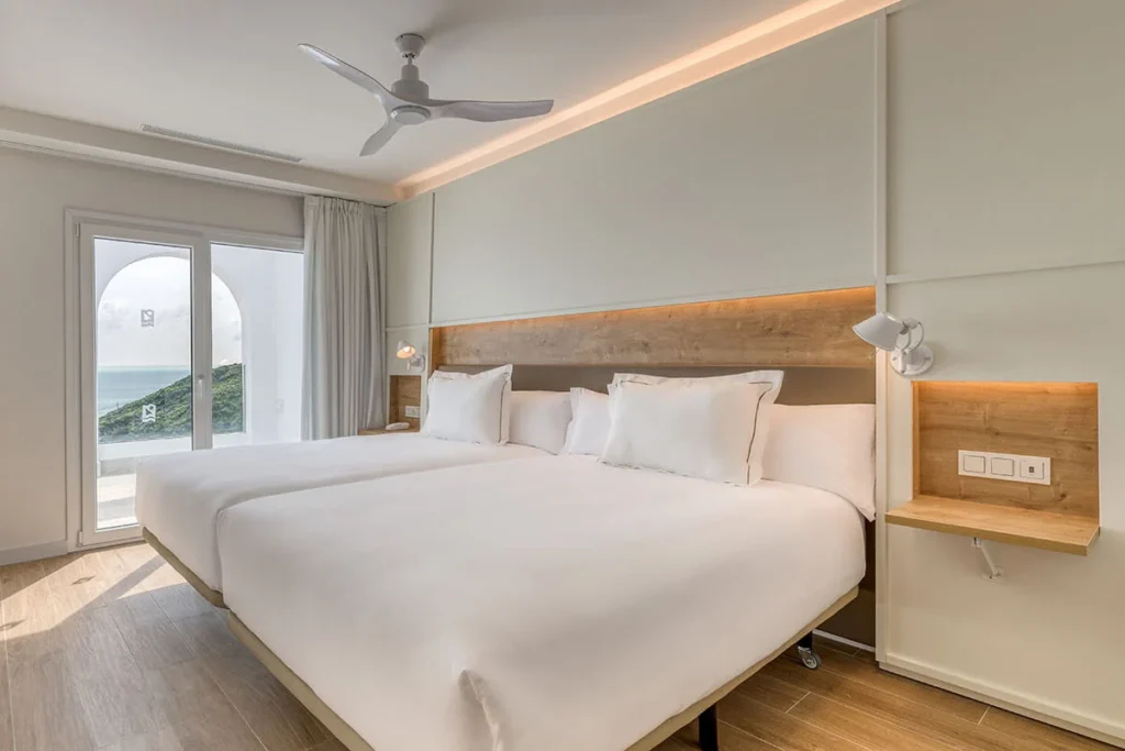 Habitaci&oacute;n moderna con cama blanca, ventilador de techo y vista al mar