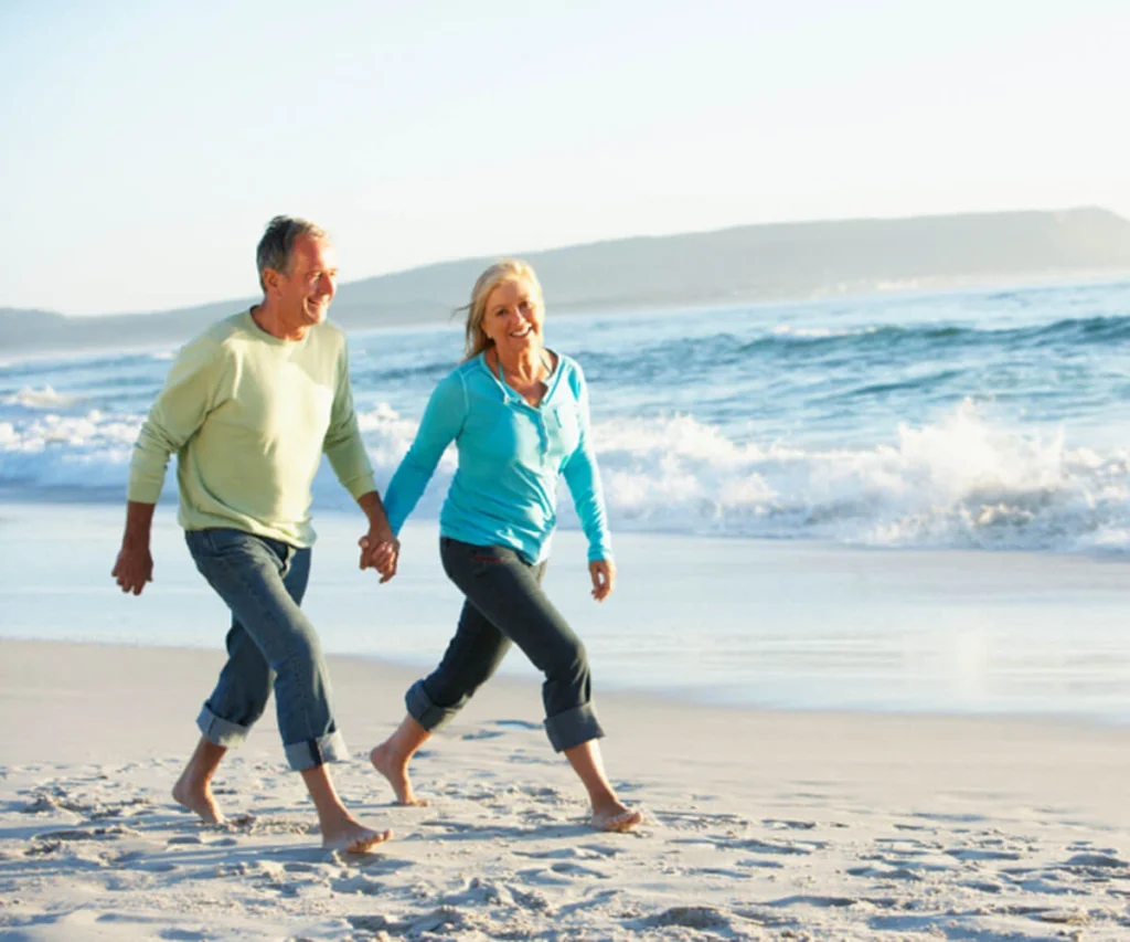 Pareja caminando descalza por la playa, junto al mar y monta&ntilde;as al fondo