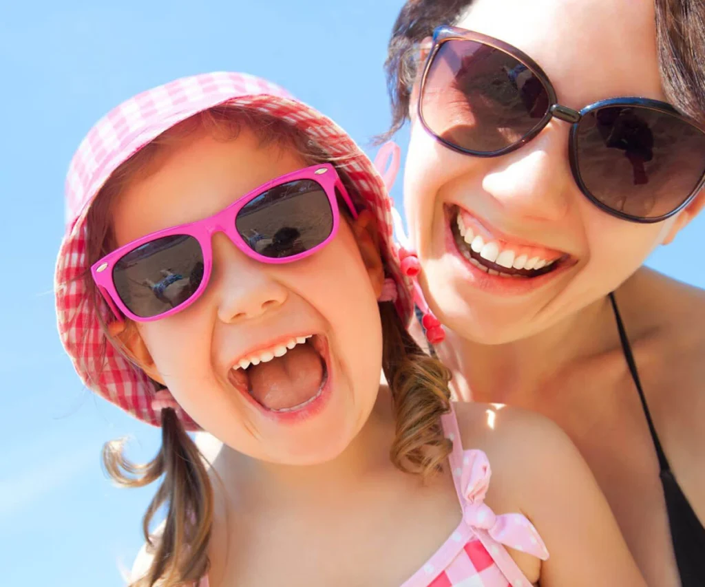 Dos chicas con sombreros y gafas de sol rosas, sonriendo al sol
