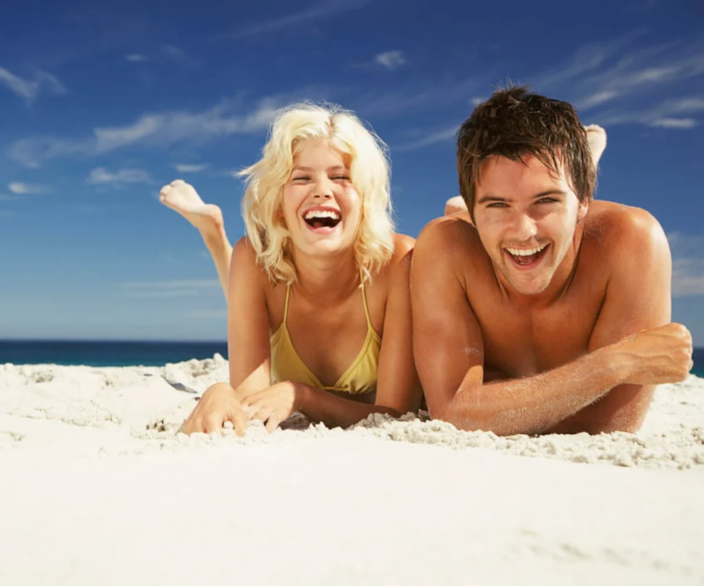 Pareja sonriendo en la playa, mujer y hombre en la arena junto al mar.