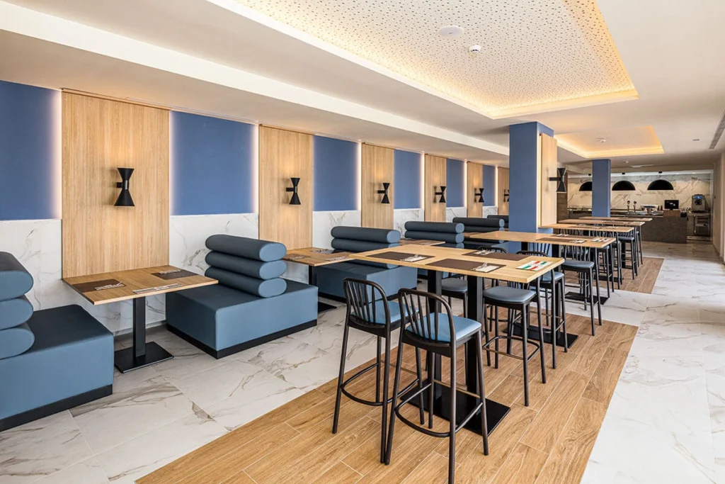Sala con mesas y taburetes, sof&aacute; azul y barra de cocina en hotel moderno