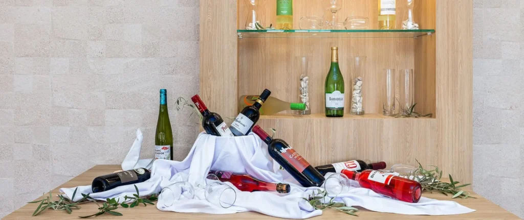 Botellas de vino sobre tela blanca y ramas verdes, junto a vitrina de madera