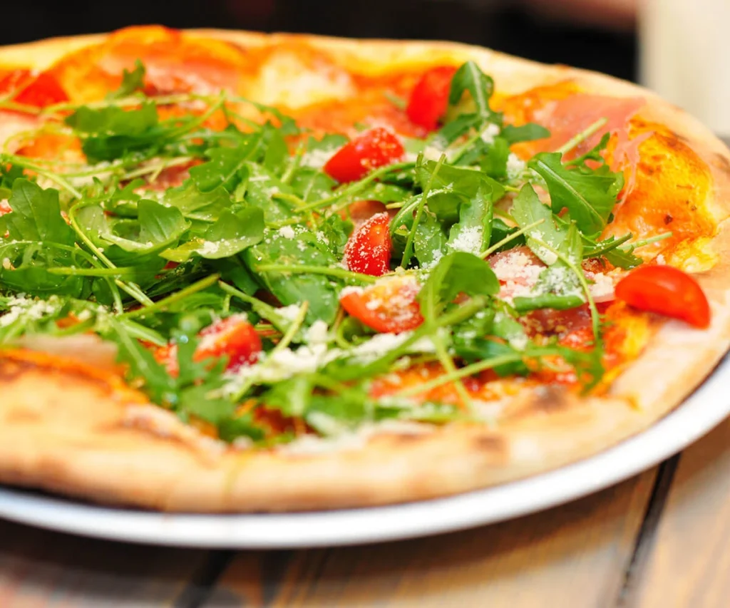 Pizza con r&uacute;cula, tomate y queso rallado sobre plato blanco