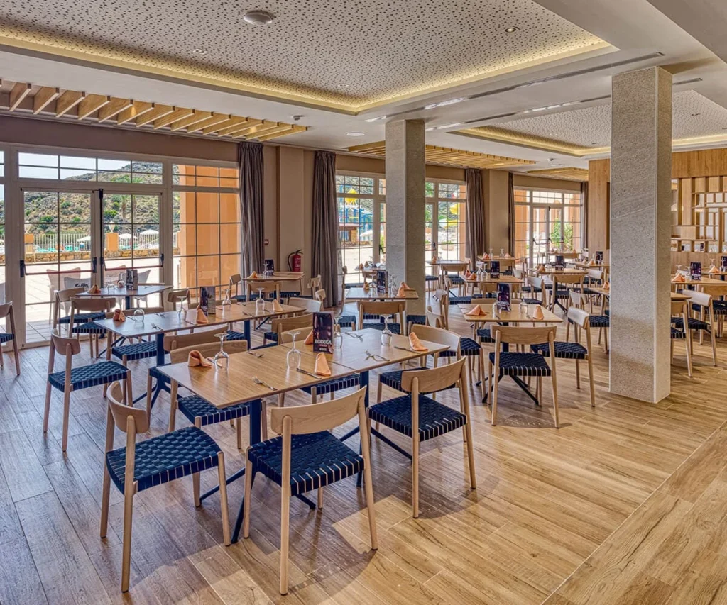 Comedor con mesas de madera y sillas, cortinas y ventanas grandes.