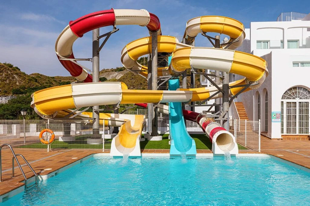 Piscina con toboganes acuáticos de colores y edificio blanco al fondo.