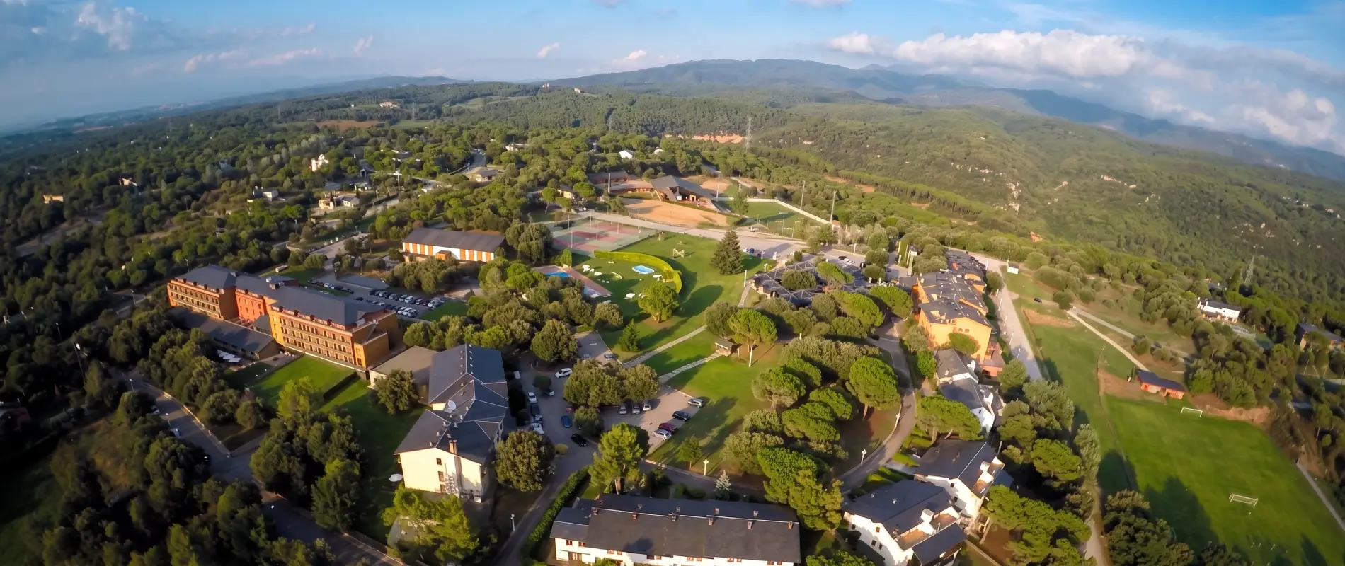 Vista a&eacute;rea de un complejo tur&iacute;stico en un valle verde, con monta&ntilde;as al fondo