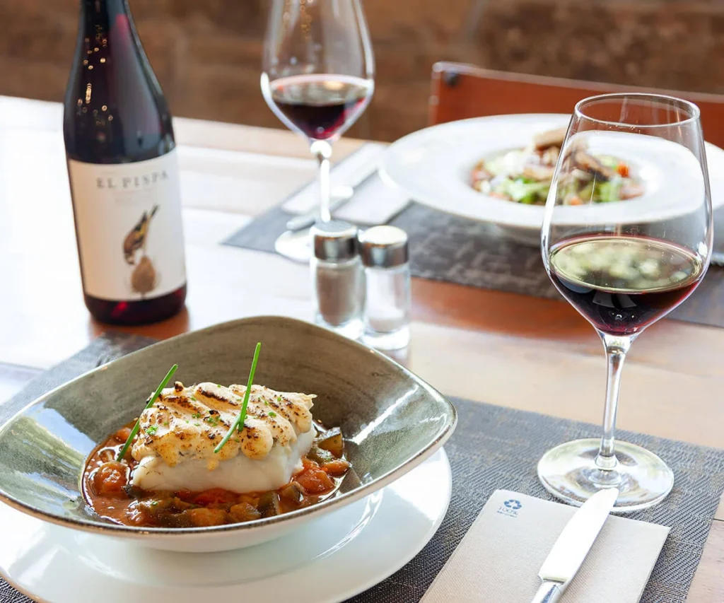 Plato de pescado con vino tinto y botella sobre mesa en restaurante
