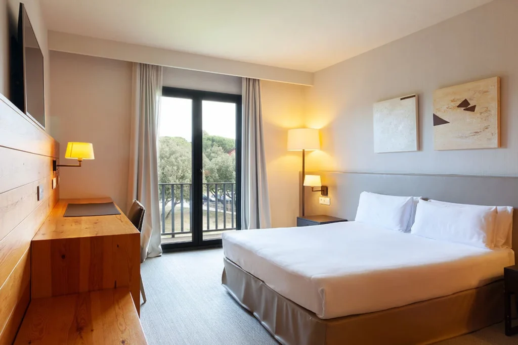 Dormitorio moderno con cama doble, l&aacute;mparas y ventanal con balc&oacute;n exterior