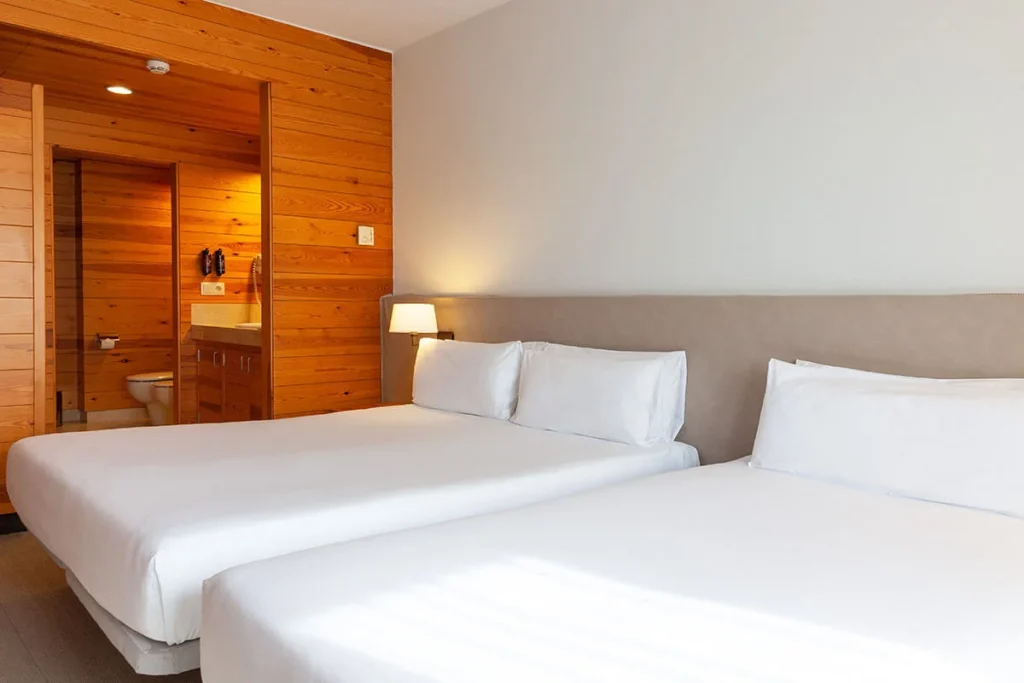 Dormitorio moderno con dos camas, l&aacute;mpara y pared de madera y espejo