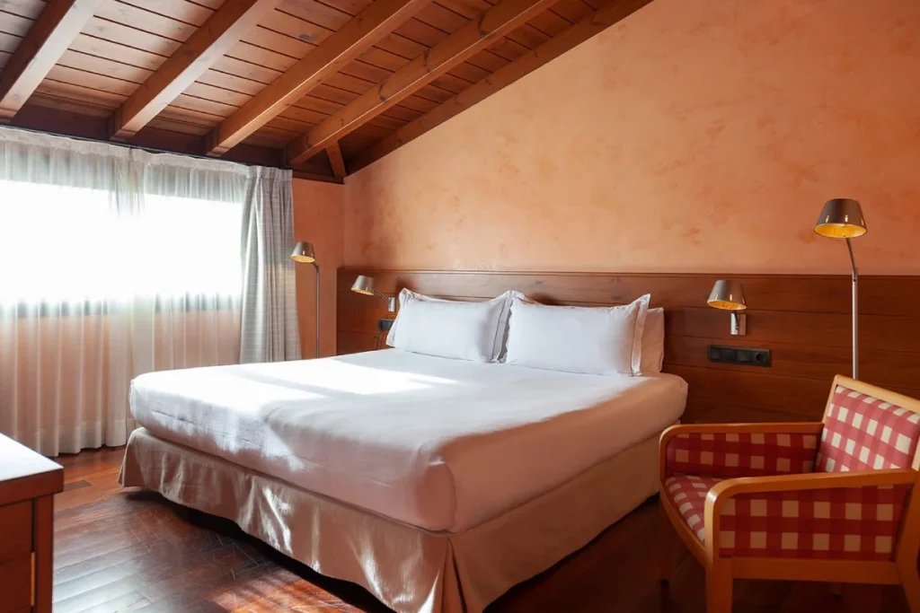 Habitaci&oacute;n de hotel con cama doble, cortinas y l&aacute;mparas de techo.