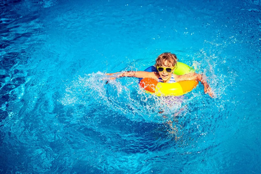 Ni&ntilde;o nadando con gafas de sol y flotador amarillo en piscina azul