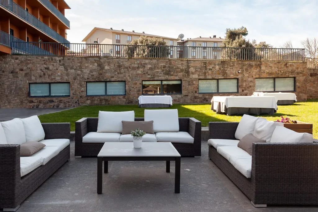 Patio con sof&aacute;s y mesas, jard&iacute;n con c&eacute;sped y muro de piedra, al aire libre