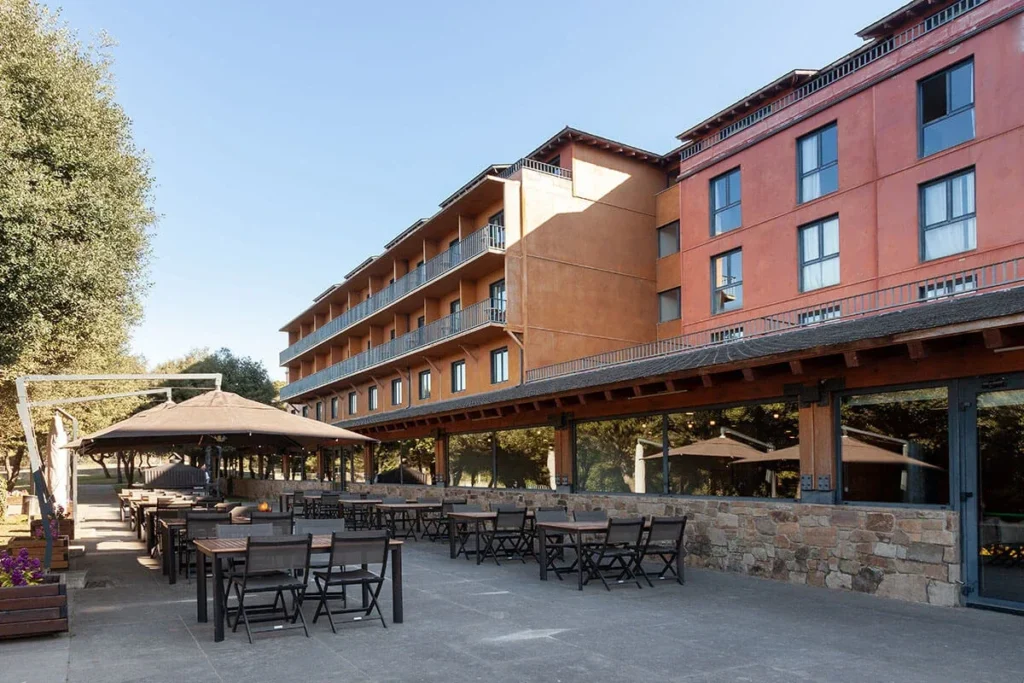 Terraza con mesas bajo sombrillas junto a un edificio hotelero de ladrillo rojo