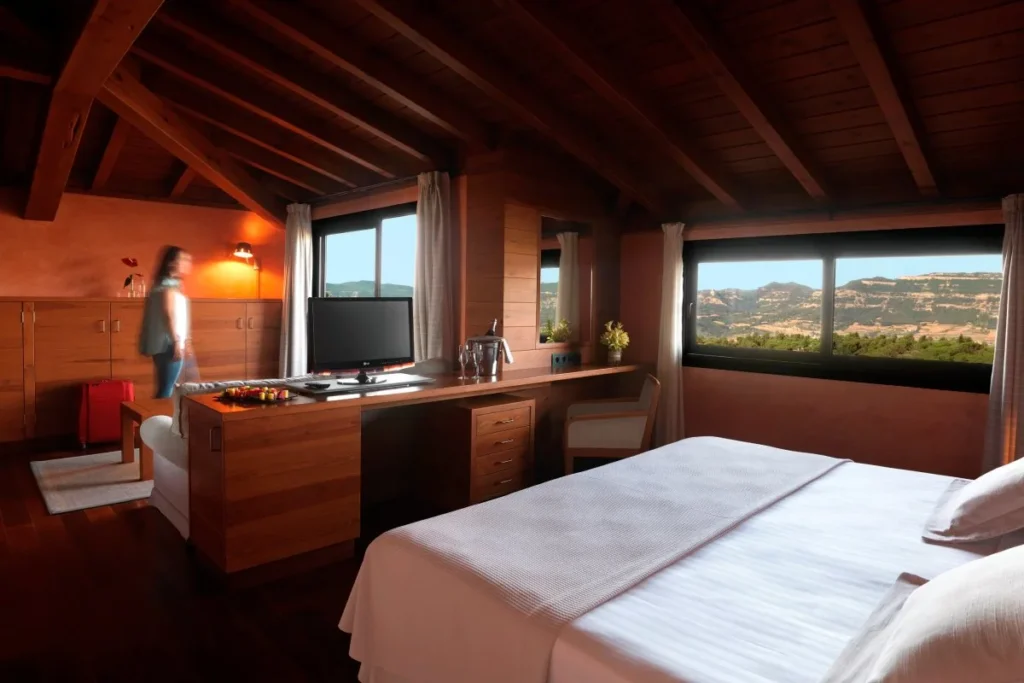 Habitaci&oacute;n de hotel con cama, escritorio y vistas a un paisaje monta&ntilde;oso.