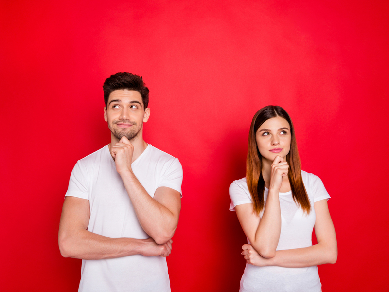 Photo of redhair girlfriend and boyfriend wondered puzzled touching their chins wearing t-shirt white isolated red vivid color background