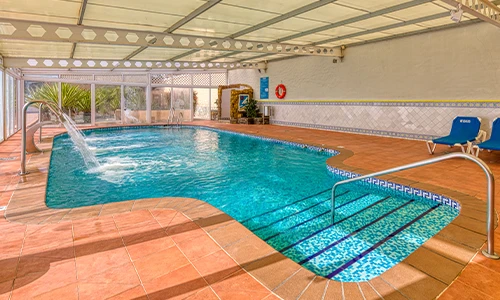 Piscina cubierta con cascada y sillas alrededor, decorada con azulejos.