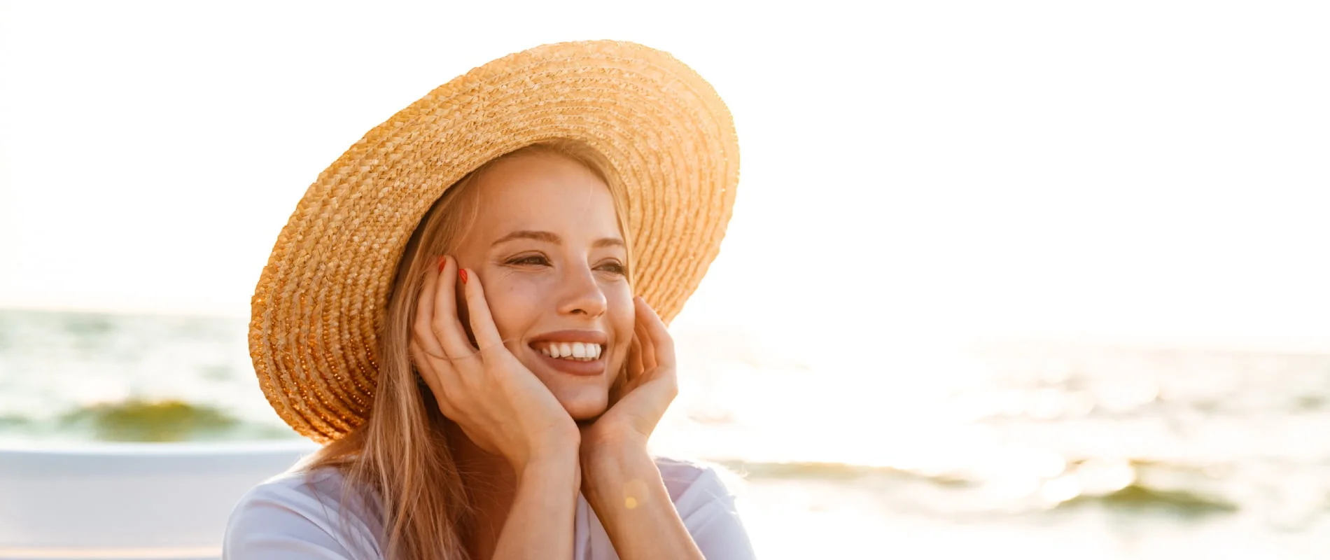 Mujer sonriente con sombrero de paja junto al mar al atardecer
