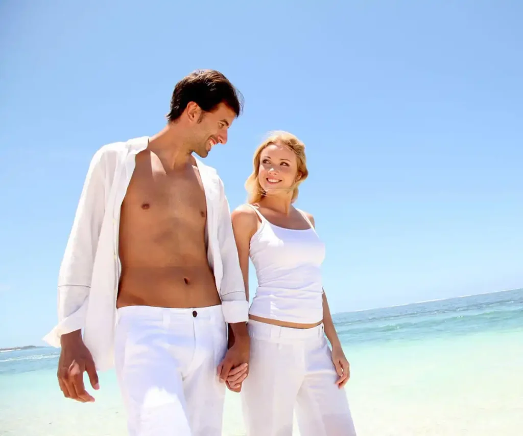 Pareja de verano con ropa blanca en la playa, mirando y sonriendo