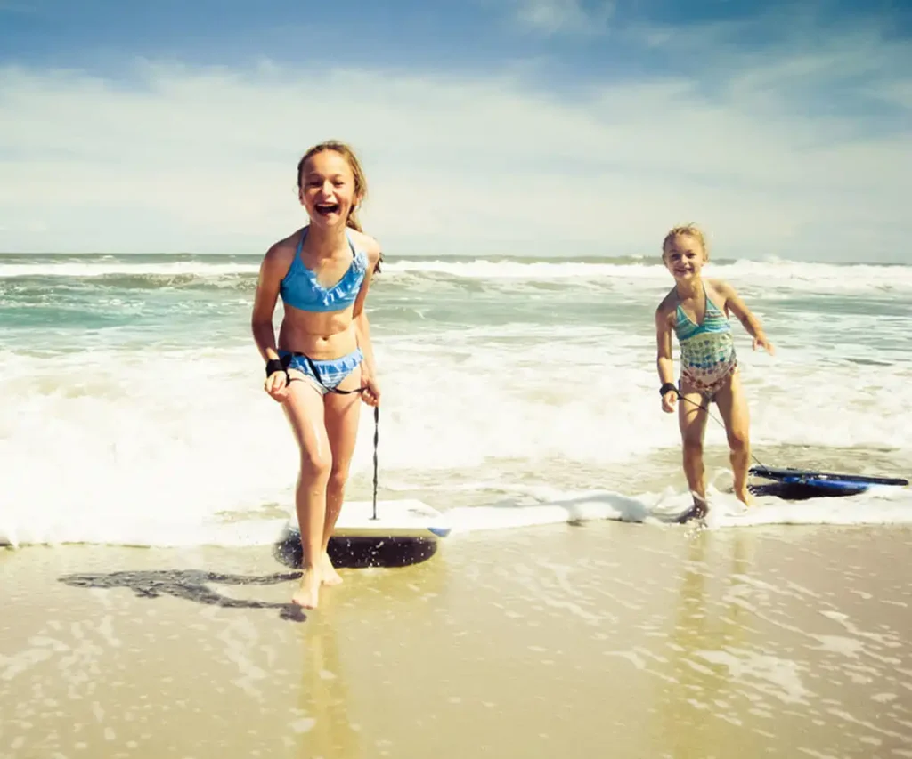 Dos ni&ntilde;as con trajes de ba&ntilde;o jugando en la playa con tablas de surf