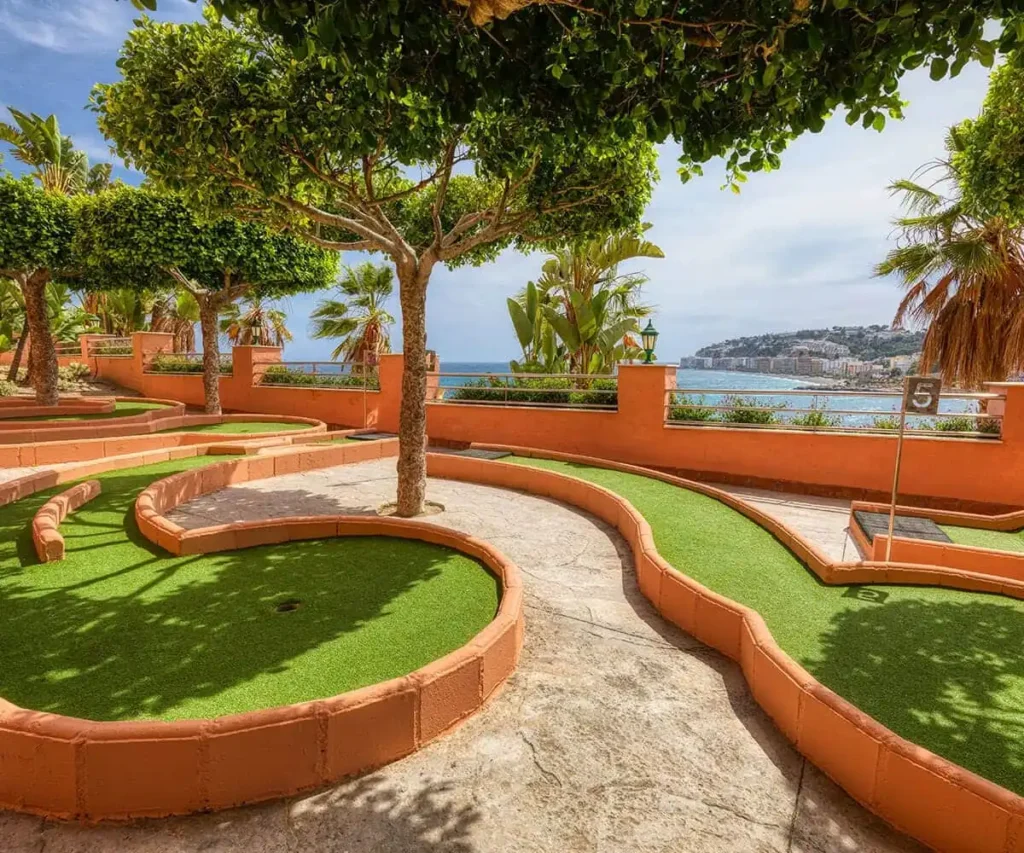 Patio con c&eacute;sped, senderos curvos y vista al mar desde un jard&iacute;n tropical