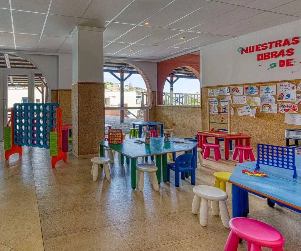 Aula infantil con mesas y sillas de colores, juegos y mural escolar