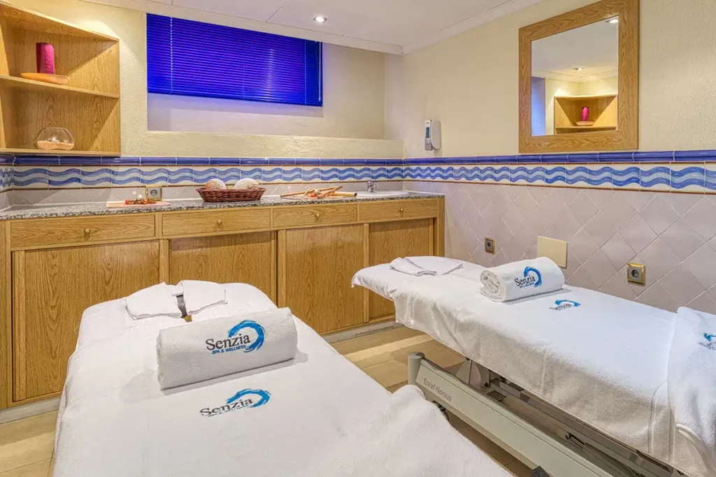 Sala de masaje con camillas blancas y toallas &ldquo;Senzia&rdquo; en un entorno moderno
