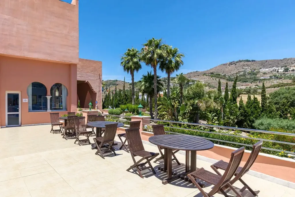 Terraza con mesa y sillas, palmeras y vista a la monta&ntilde;a bajo cielo azul
