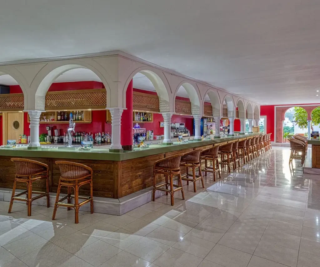 Barra de bebidas en sal&oacute;n con arcos blancos y sillas altas de madera