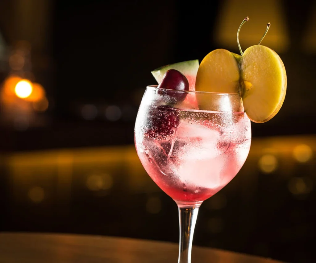 C&oacute;ctel rojo con hielo en copa, decorado con uvas y rodajas de fruta