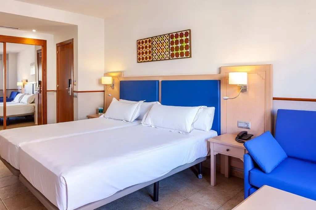 Habitaci&oacute;n de hotel con cama blanca, cabecero azul y sof&aacute; azul