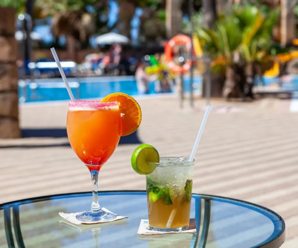 Dos cocteles con hielo y rodajas de c&iacute;tricos junto a una piscina al aire libre