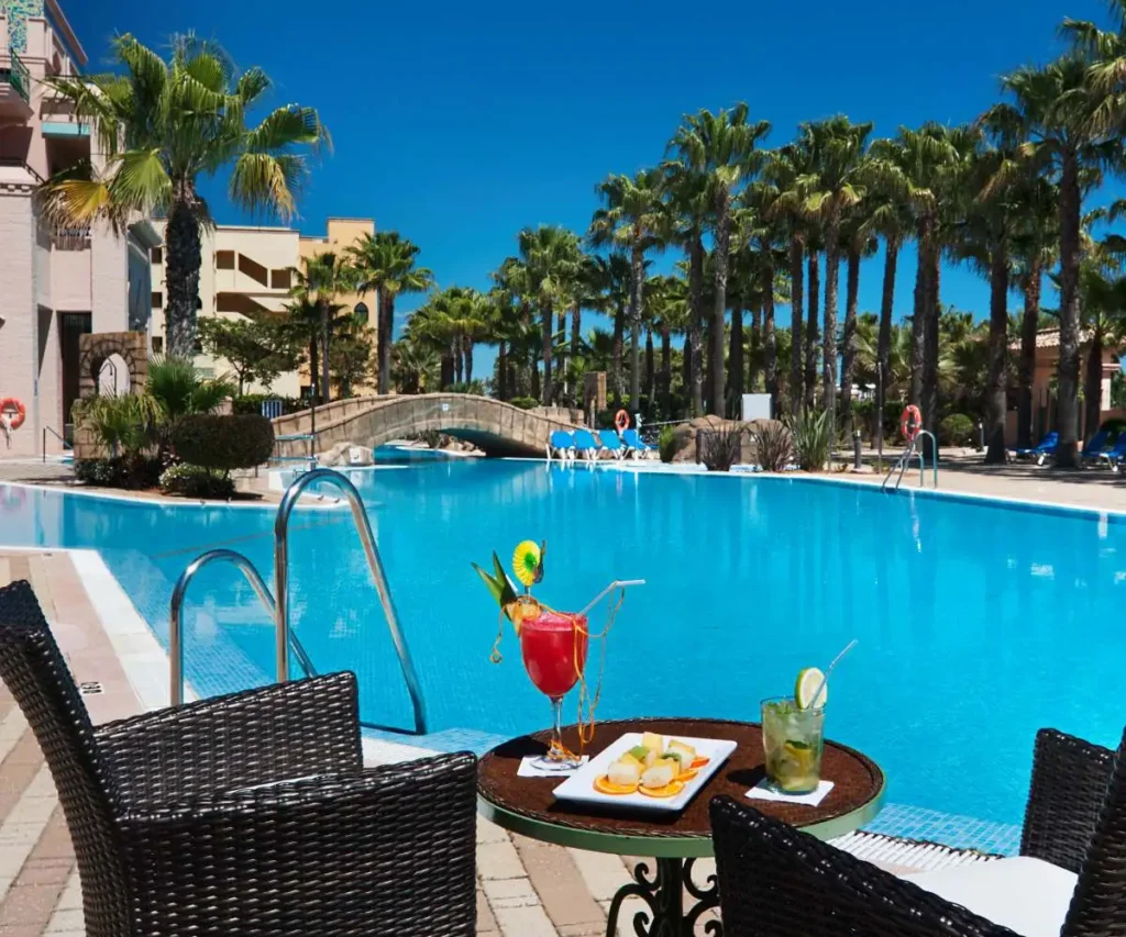 Piscina azul con palmeras y mesa con bebida y copa tropical en el resort