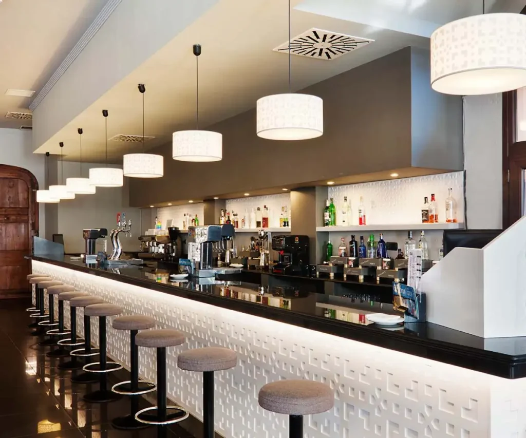 Bar con barra iluminada, botellas y taburetes en un interior moderno