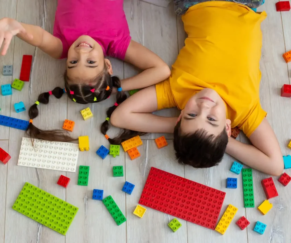 Dos ni&ntilde;os jugando con piezas tipo LEGO sobre el suelo, en vista cenital