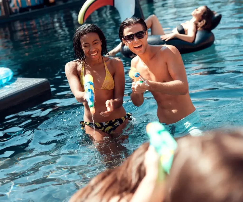 Pareja sonriente en la piscina con juguetes, un ni&ntilde;o al fondo.
