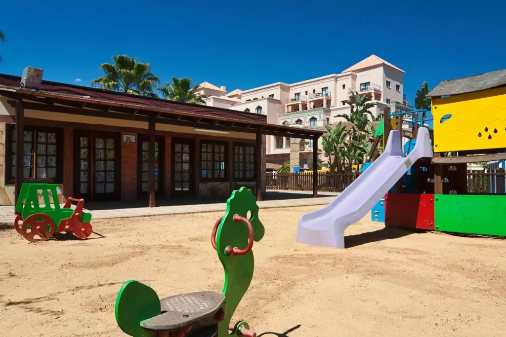 Parque infantil con tobog&aacute;n y juegos verdes en patio soleado