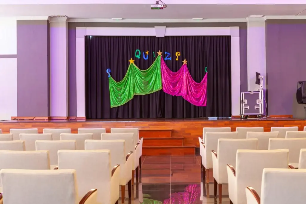 Escenario con tel&oacute;n y arco de luces verde, rosa y texto &ldquo;QDJZQ&rdquo;.